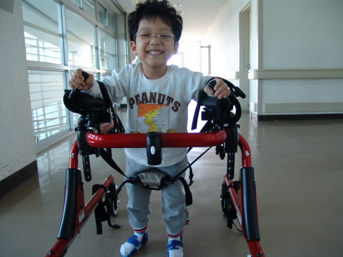 여섯살 정훈이가 경기도재활공학서비스연구지원센터에서 대여받은 보행보조기구를 이용해 걷기 연습을 하며 환하게 웃고 있다.