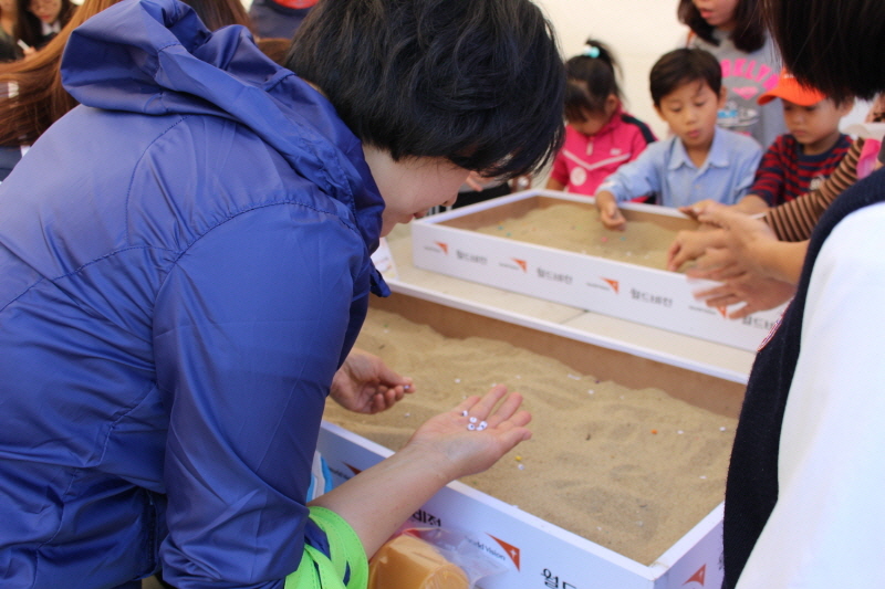 월드비전 경기지부의 ‘아동노동-팔찌를 만들어 하루를 살아보기’ 행사. 모래판에서 구슬을 찾고 있는 참가자들.