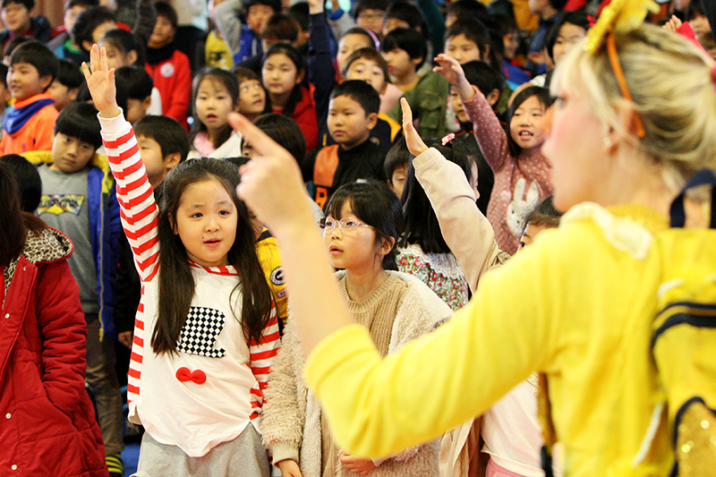우정초교 학생들이 영어 질문을 듣고 정답을 맞히려고 손을 들고 있다.