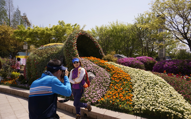 색색의 꽃들이 마치 물줄기를 연상시키는 조형물 앞에서 한 부부가 사진을 찍고 있다.