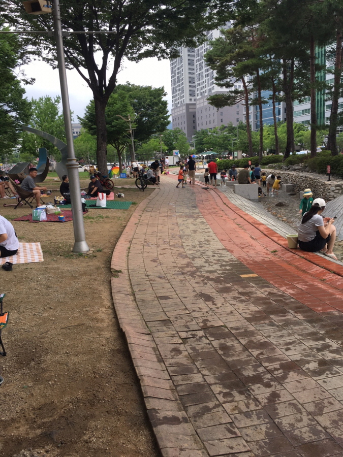 나무 그늘 속에서 돗자리를 펴고 앉아있는 시민들, 바닥분수에서 더위를 식히는 시민들  